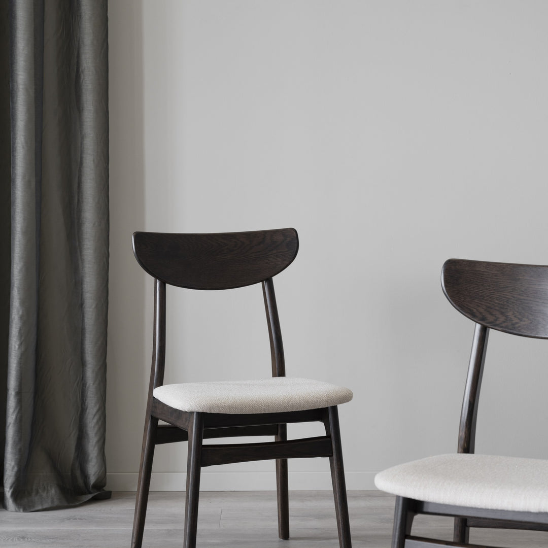 Rowico Rodham spisestol i brun eik med lyst beige setetrekk, to stoler ved grått gardin i lyst rom