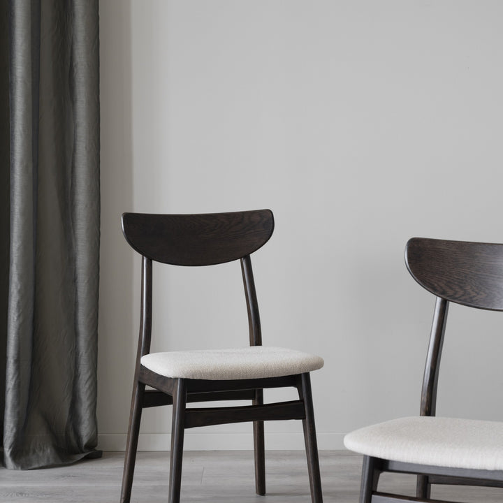 Rowico Rodham spisestol i brun eik med lyst beige setetrekk, to stoler ved grått gardin i lyst rom