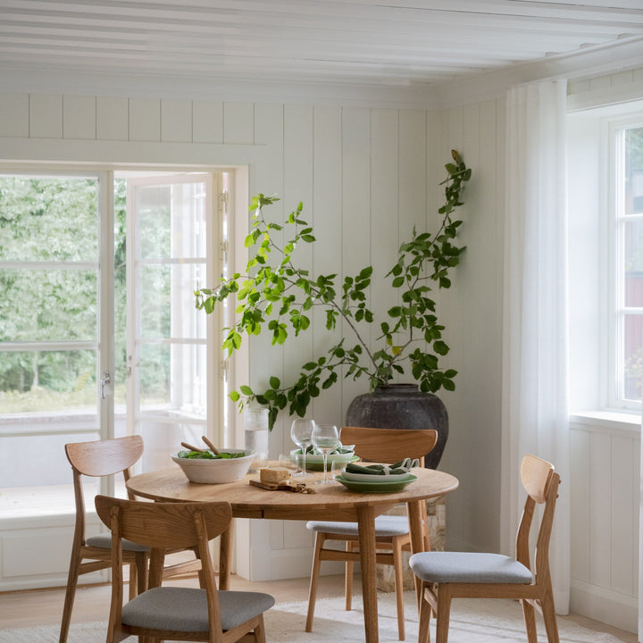 Rowico Rodham spisestoler i eik med gråbeige sete ved rundt eikebord i lyst panelrom med stor grønn grein