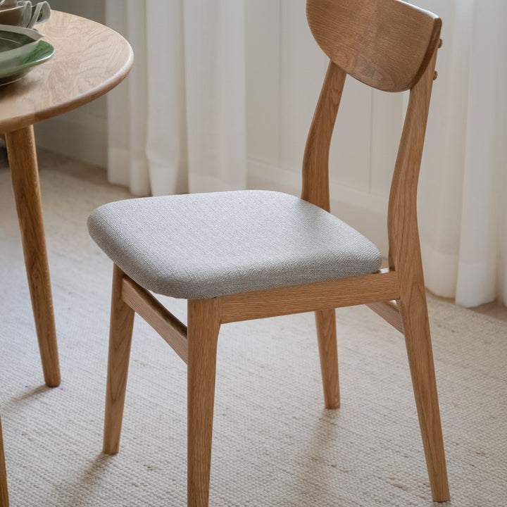 Rowico Rodham spisestol i eik med gråbeige stoffsete, ved rundt eikebord på beige teppe i lyst rom