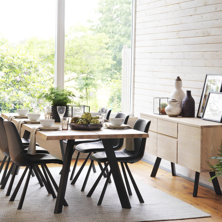 Rowico Auburn spisestol i sort kunstskinn ved lyst spisebord i lyst rom med vindu og planter