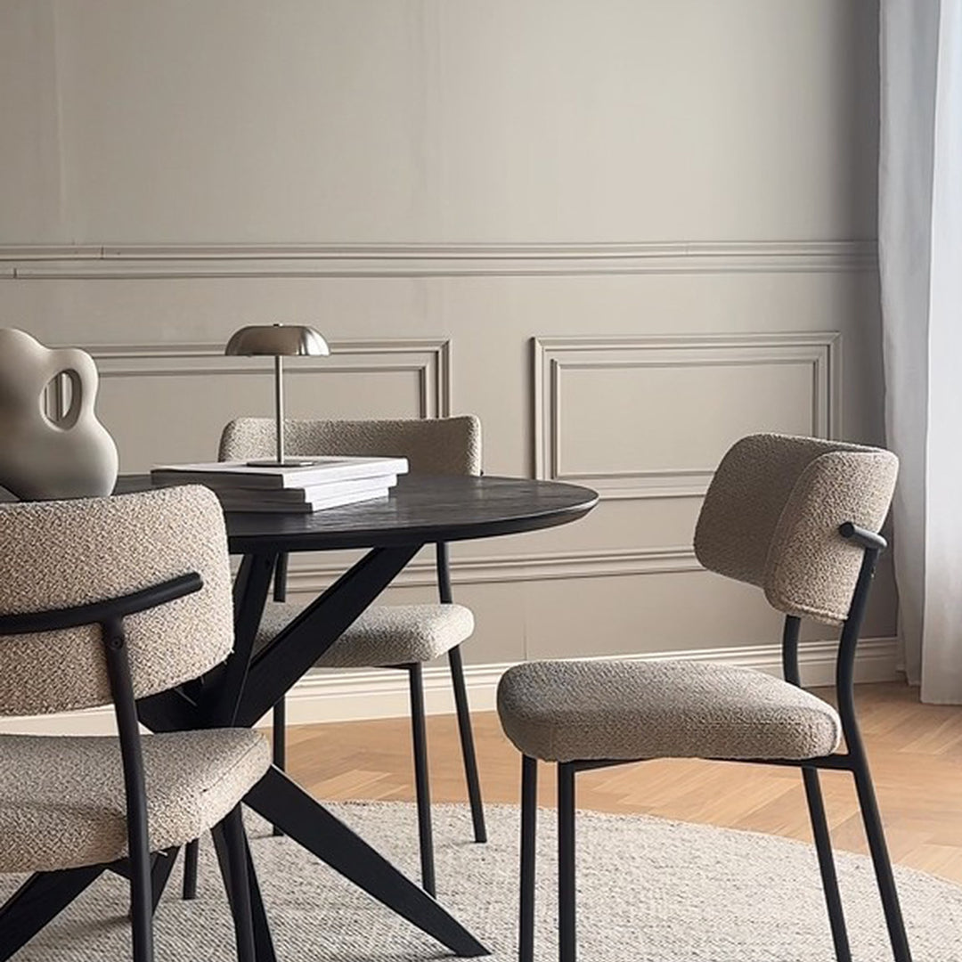 Rowico Herbster spisestol i beige bouclé rundt svart spisebord med bordlampe mot lys panelvegg