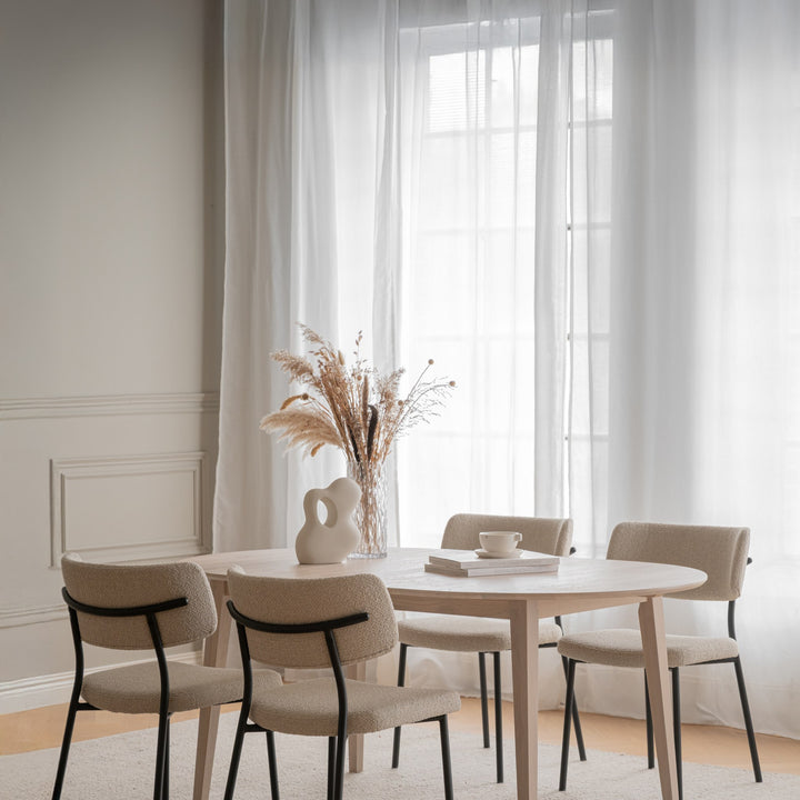 Rowico Herbster spisestol i beige bouclé rundt lyst spisebord ved vindu med tørket pampasgress