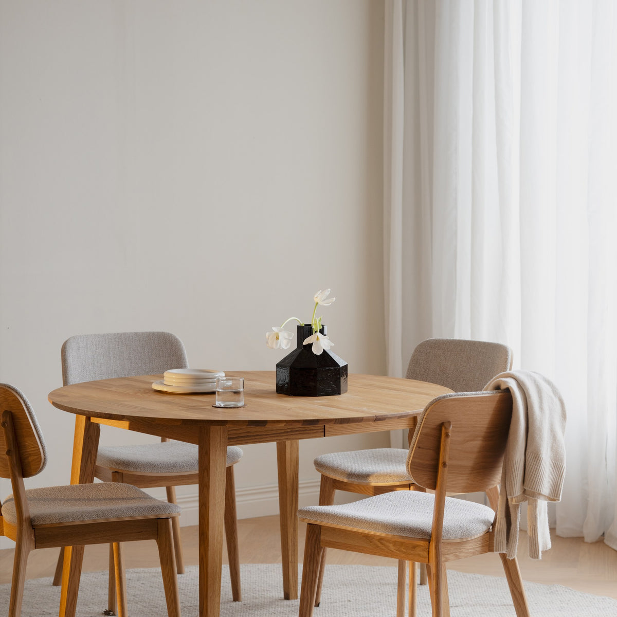 Rowico Barrett spisestoler i beige stoff ved rundt eikebord med vase og pledd i lyst rom
