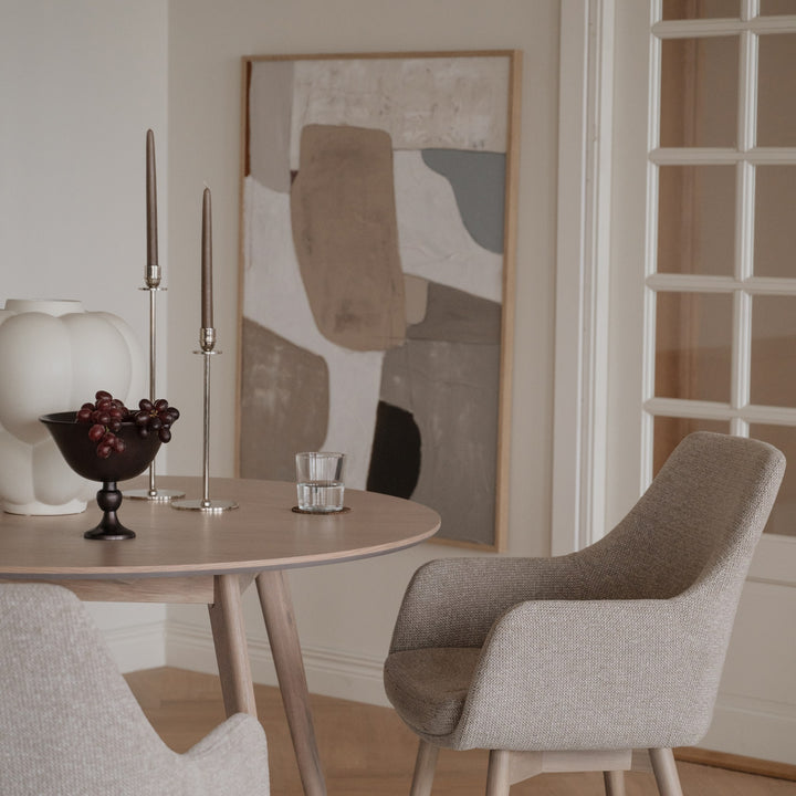 Rowico Denley spisestol i beige stoff ved lyst rundt eikebord med kunst og dekor