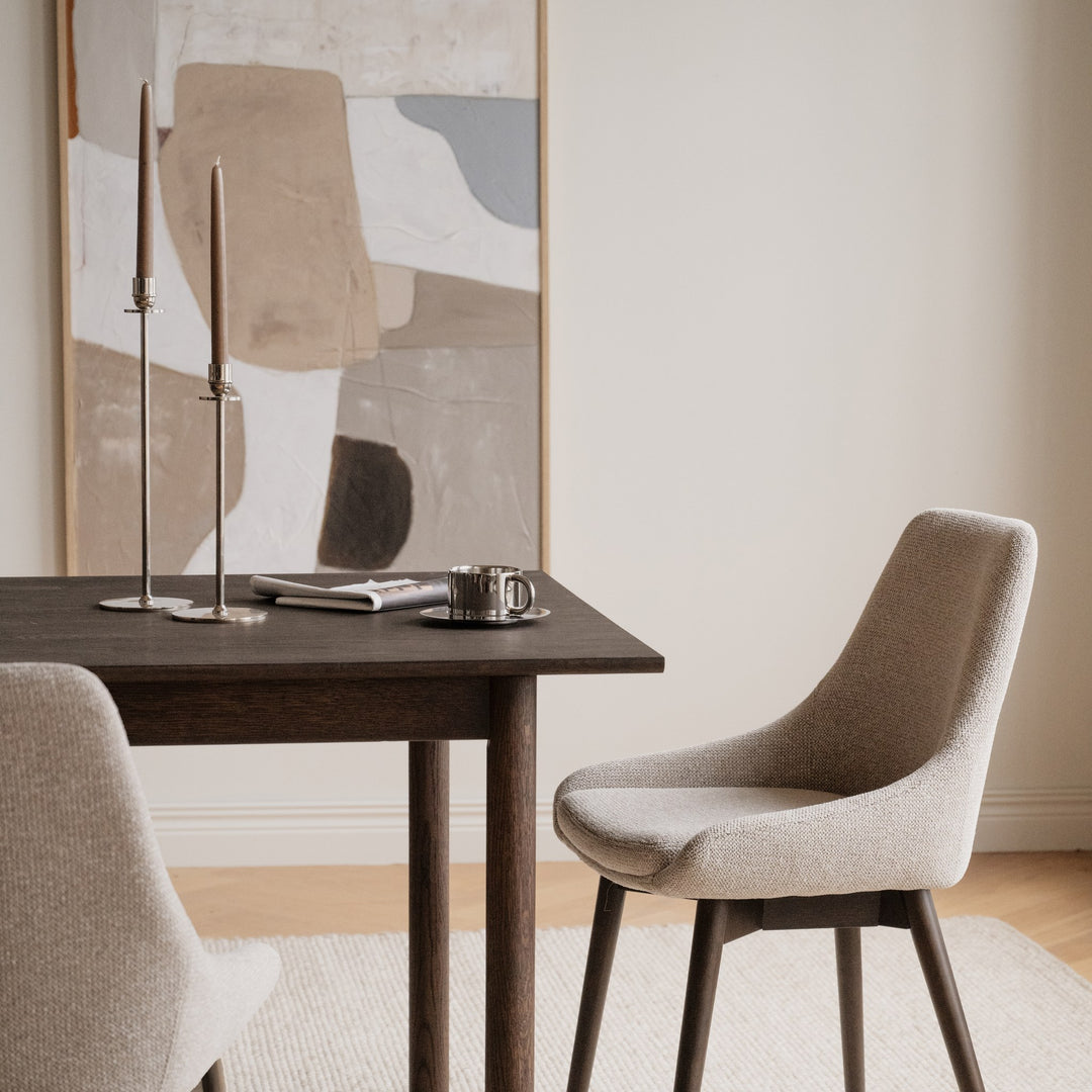 Rowico Denley spisestol i lys beige stoff ved mørkt eikebord i lys spisestue med kunst