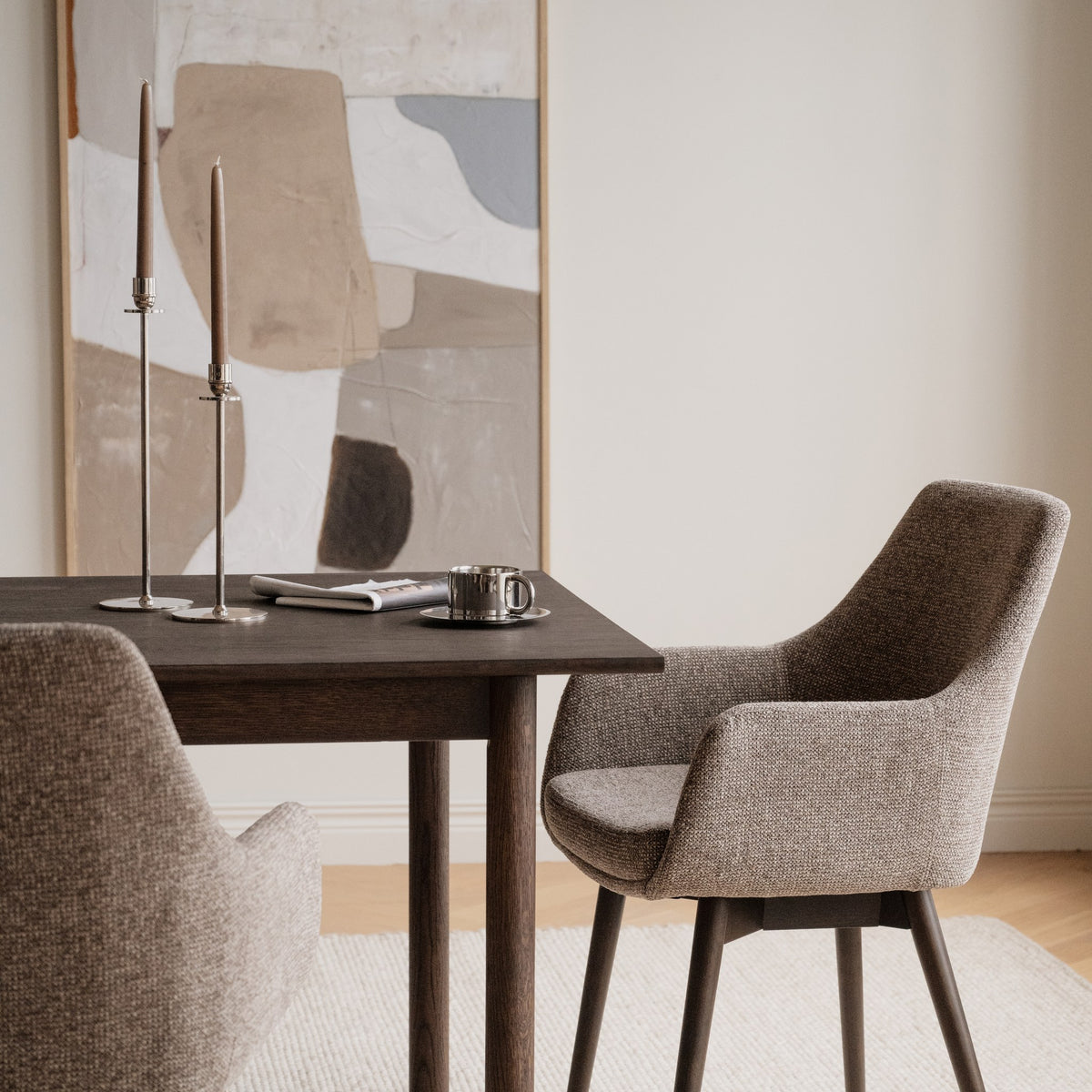 Rowico Denley spisestol i gråbeige stoff med armlener ved mørkt eikebord med kunst