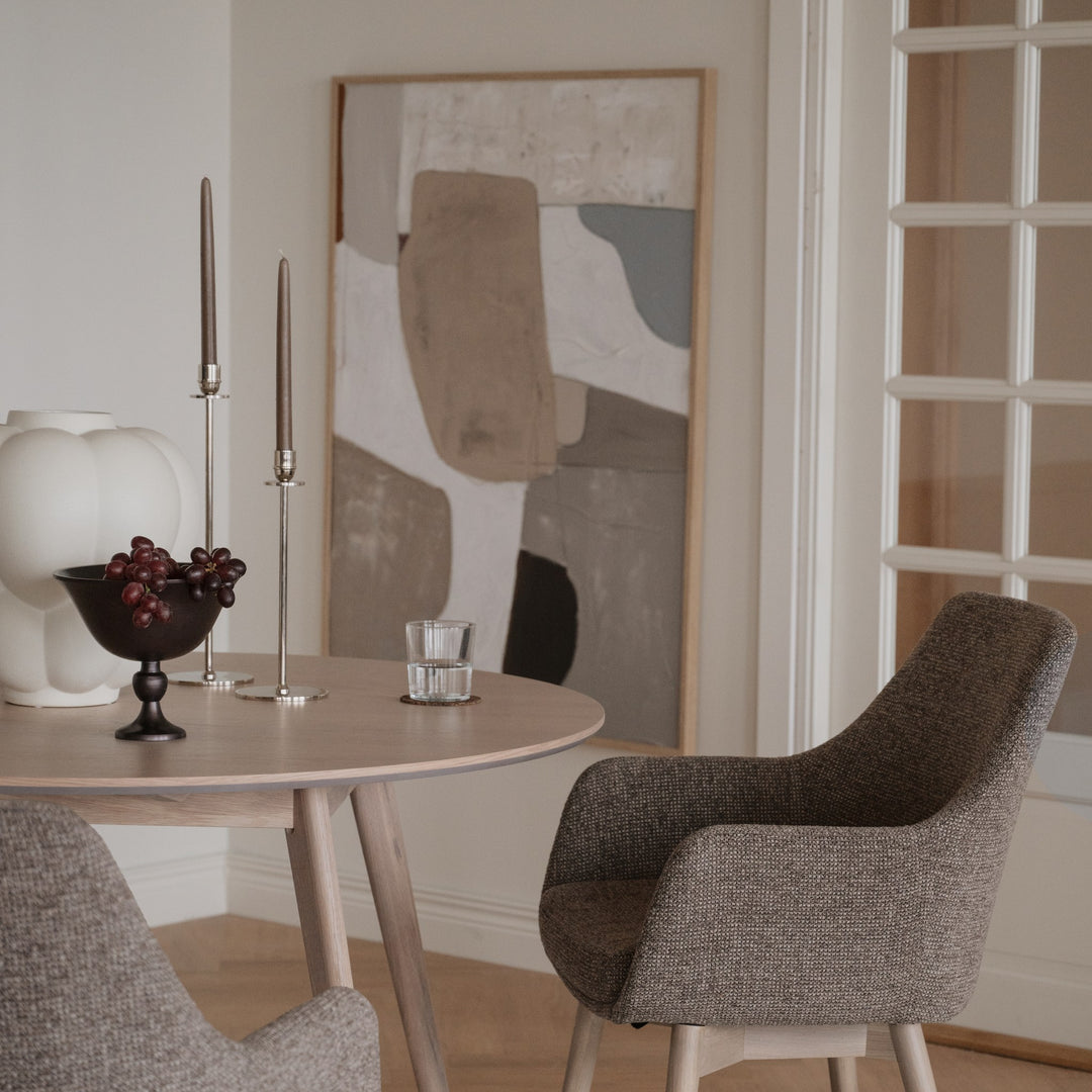 Rowico Denley spisestol i gråbrun stoff med armlener ved lyst rundt eikebord med kunst