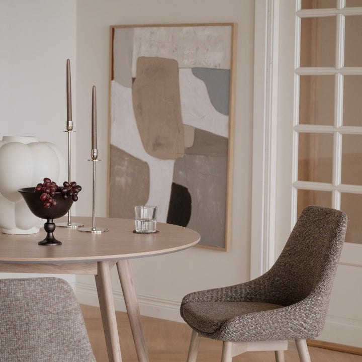 Rowico Denley spisestol i gråbrun stoff ved lyst rundt eikebord med kunst og vindusdør