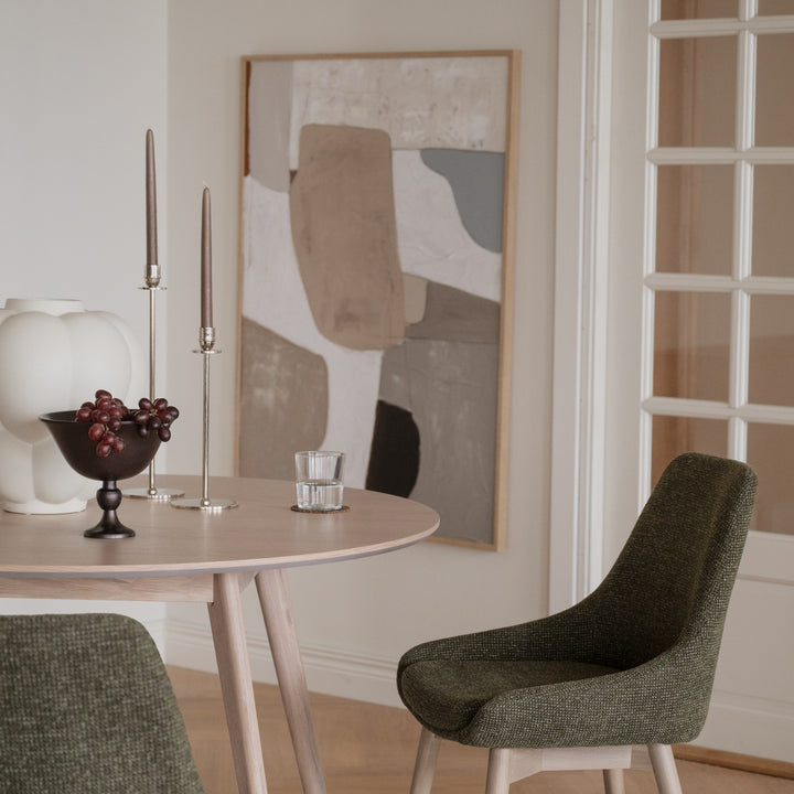 Rowico Denley spisestol i mørkegrønn stoff ved lyst rundt eikebord med kunst og vindusdør