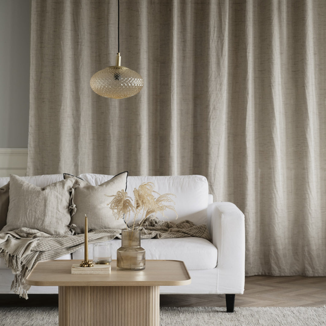 Rowico Sullivan sofabord i lys eik foran hvit sofa med beige gardiner og lampe