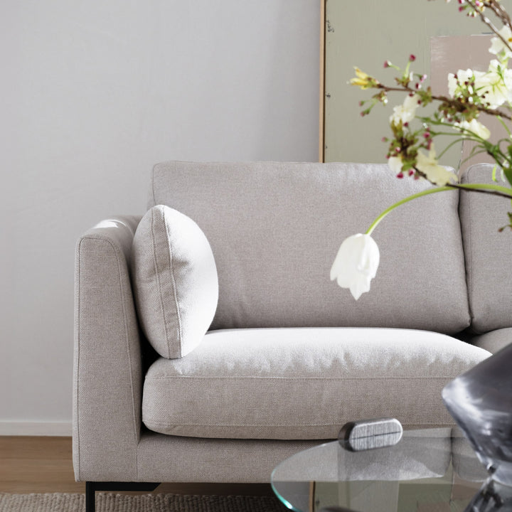Rowico Arran sofabord i glass skimtes ved hjørnet av lys beige sofa med pute og hvit tulipan