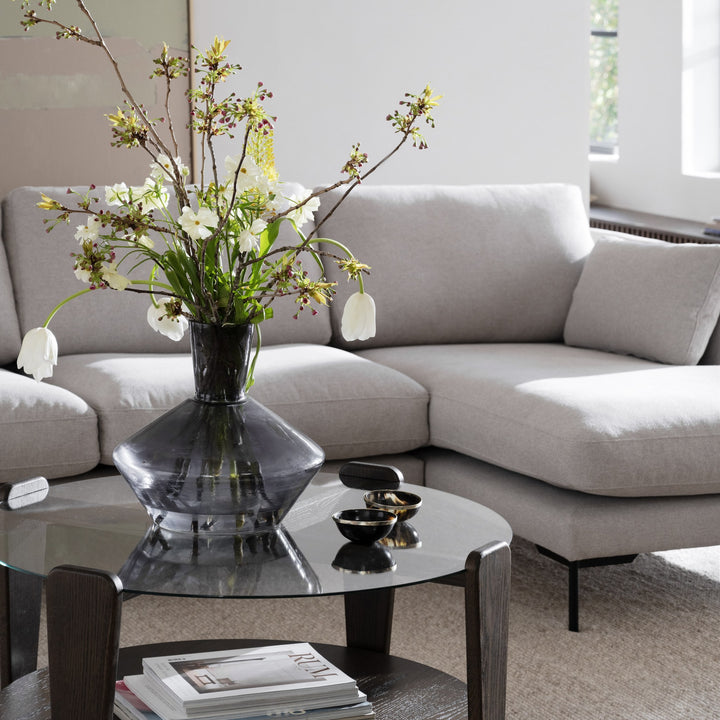 Rowico Arran sofabord i glass og mørk eik med magasiner, foran lys beige sofa og røykfarget vase