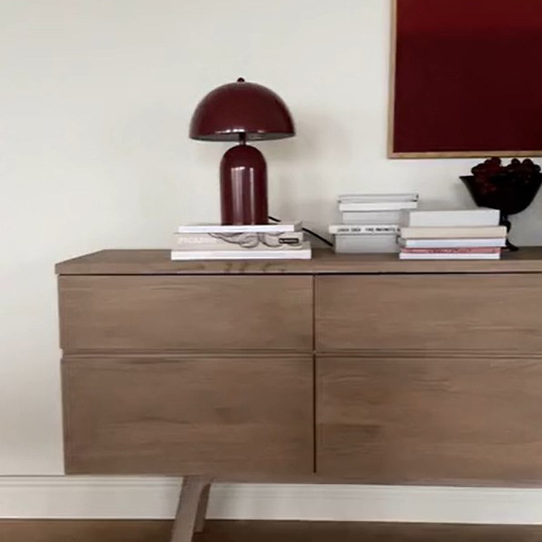 Rowico Cleardale skjenk i sandfarget eik med vinrød lampe og bøker, mot hvit vegg og rød kunst