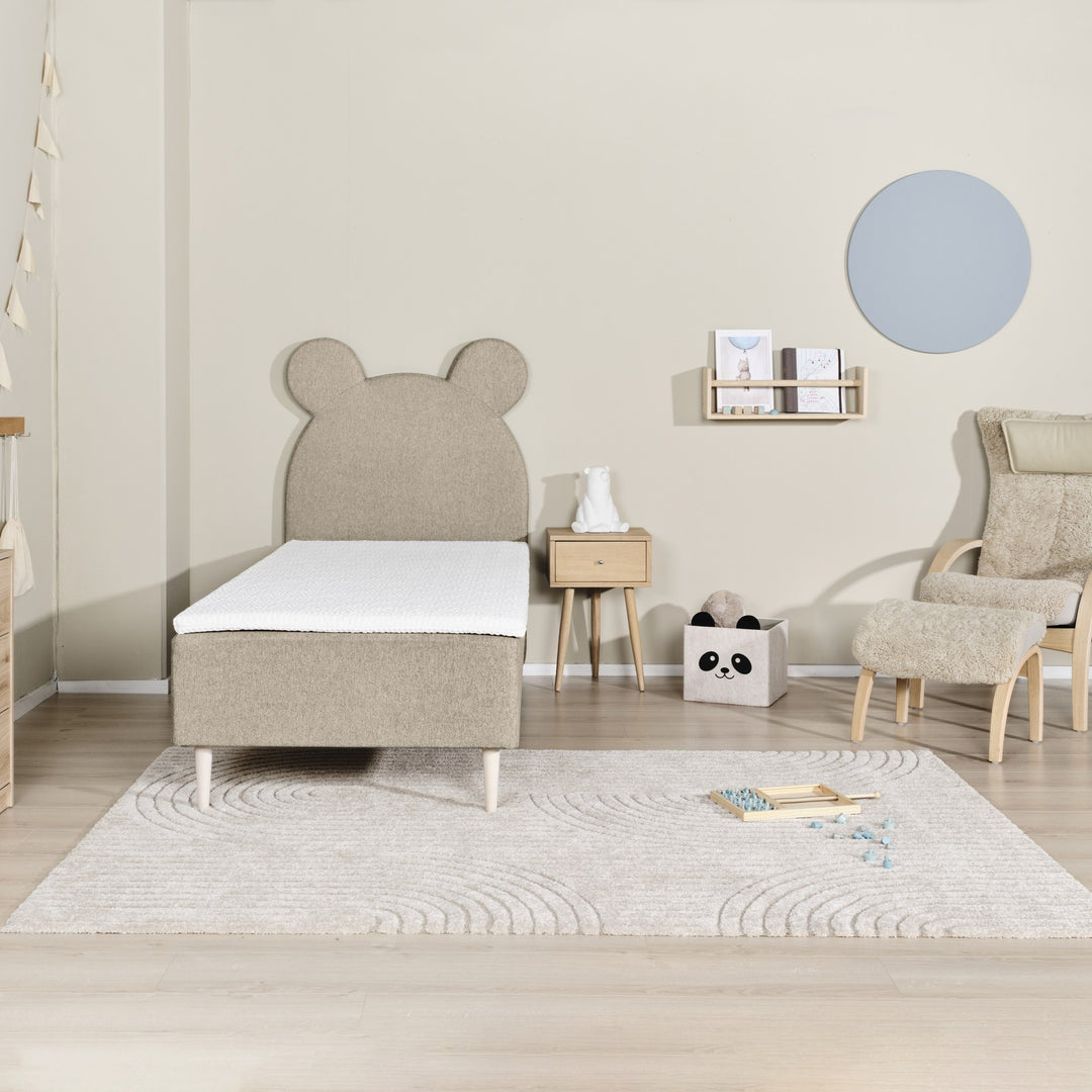 Asleep Teddy sengegavl i beige i lyst barnerom med teppe, pandakurv og saueskinnstol