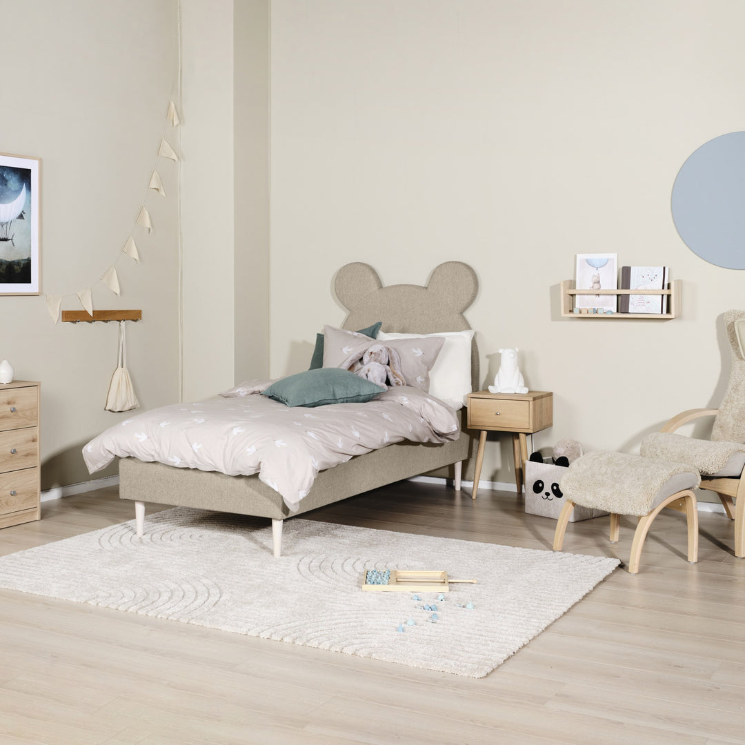 Asleep Teddy sengegavl i beige i lyst barnerom med kommode, teppe og saueskinnstol