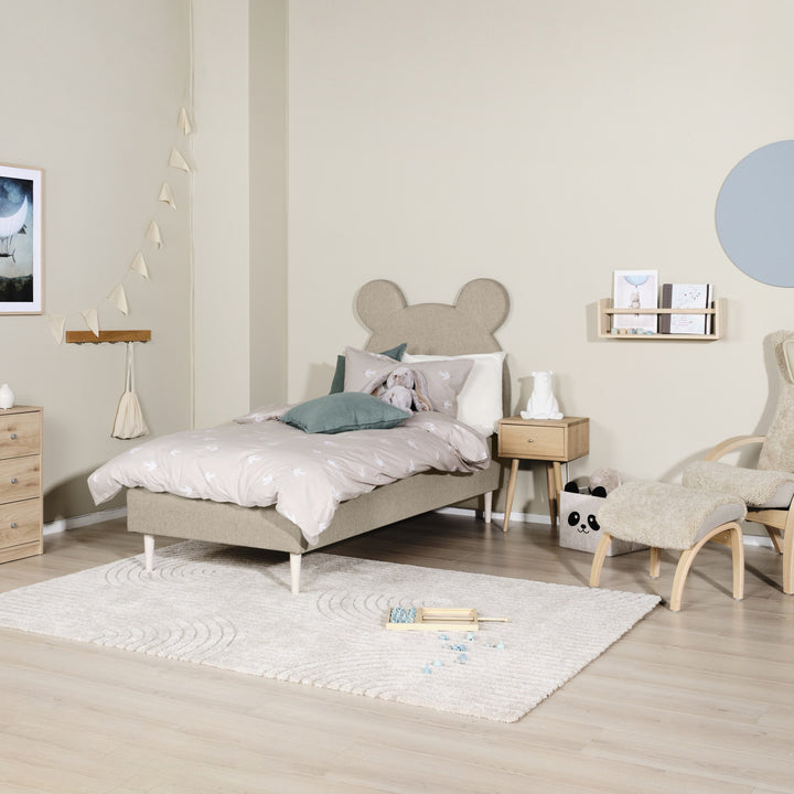 Asleep Teddy sengegavl i beige i lyst barnerom med kommode, teppe og saueskinnstol