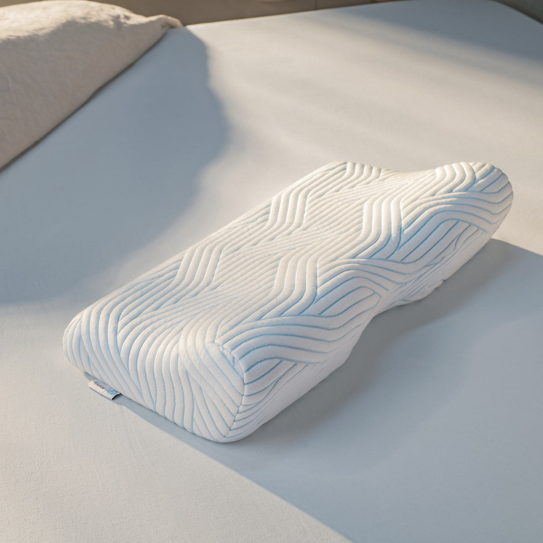 TEMPUR ErgoPlus SmartCool hodepute med dyp ergonomisk fasong og blått bølgemønster på hvit seng