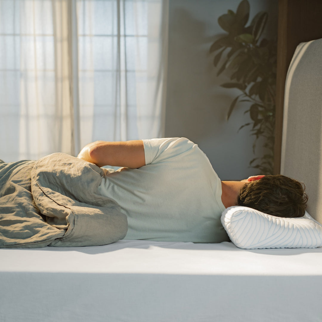 Tempur ErgoPlus SmartCool hodepute under mann som sover på siden mot beige sengegavl med plante