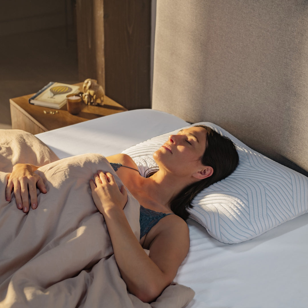 Tempur SmartCool Symphony hodepute under kvinne som sover på rygg mot beige sengegavl med nattbord