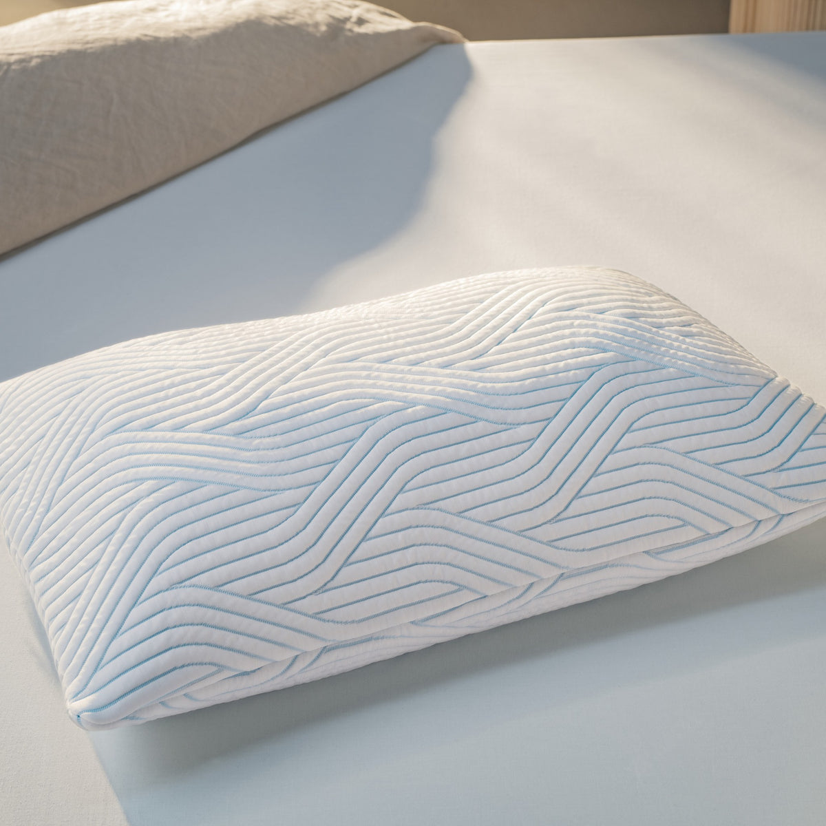 Tempur SmartCool Comfort hodepute, myk og høy med blått bølgemønster på lys seng