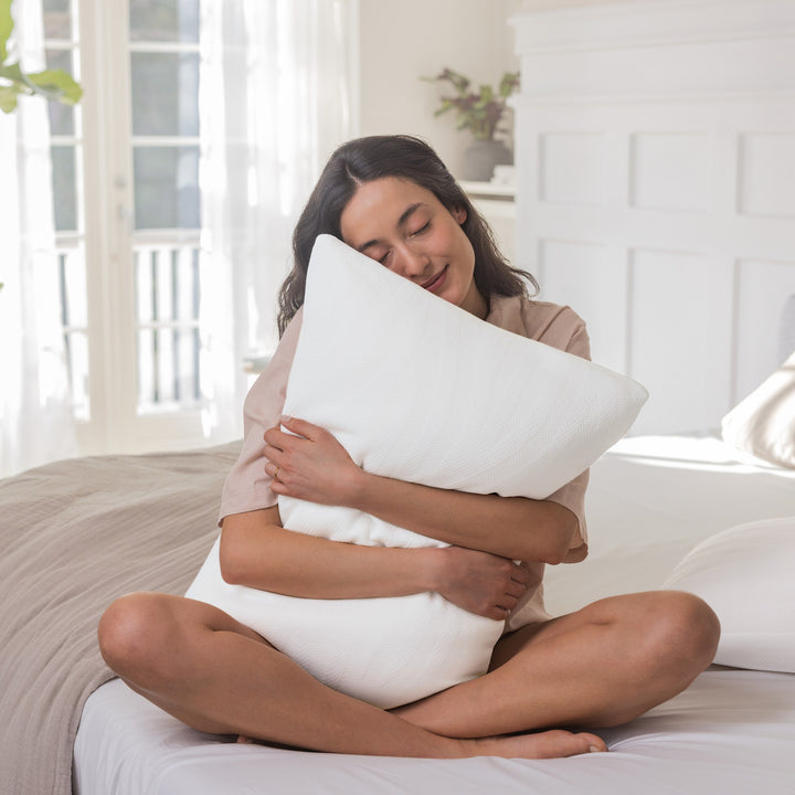 Tempur Comfort PureClean hodepute i hvitt, kvinne sitter på sengen og klemmer puten i lyst soverom