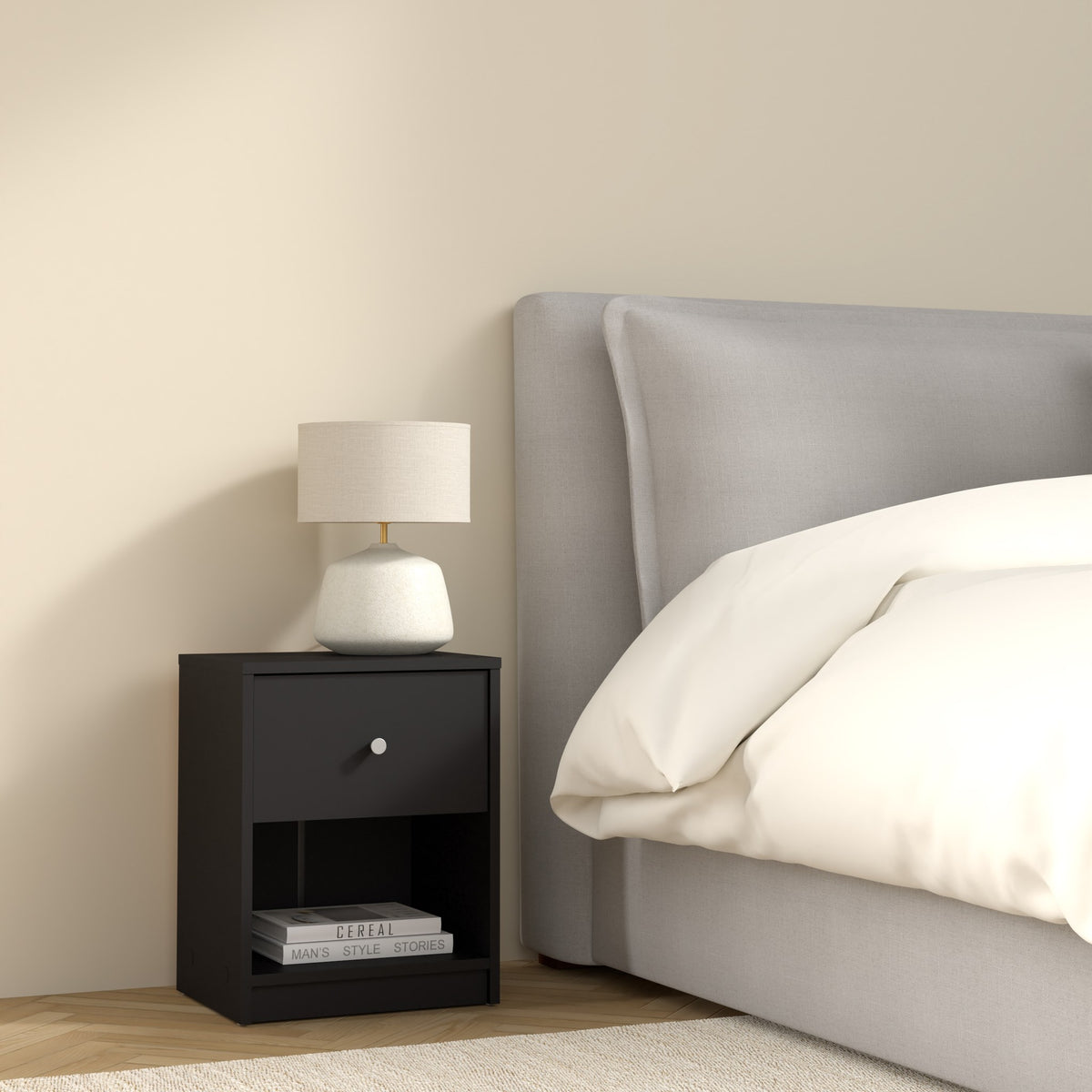 May nattbord i sort med skuff og åpen hylle, med lampe ved grå seng i soverom