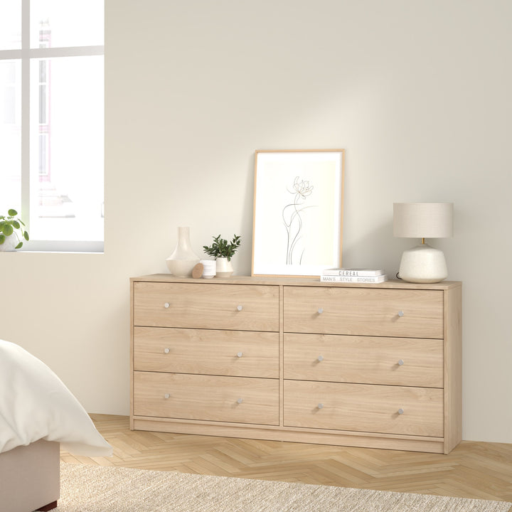 May kommode i lys eik med seks skuffer, med bilde, plante og bordlampe i soverom