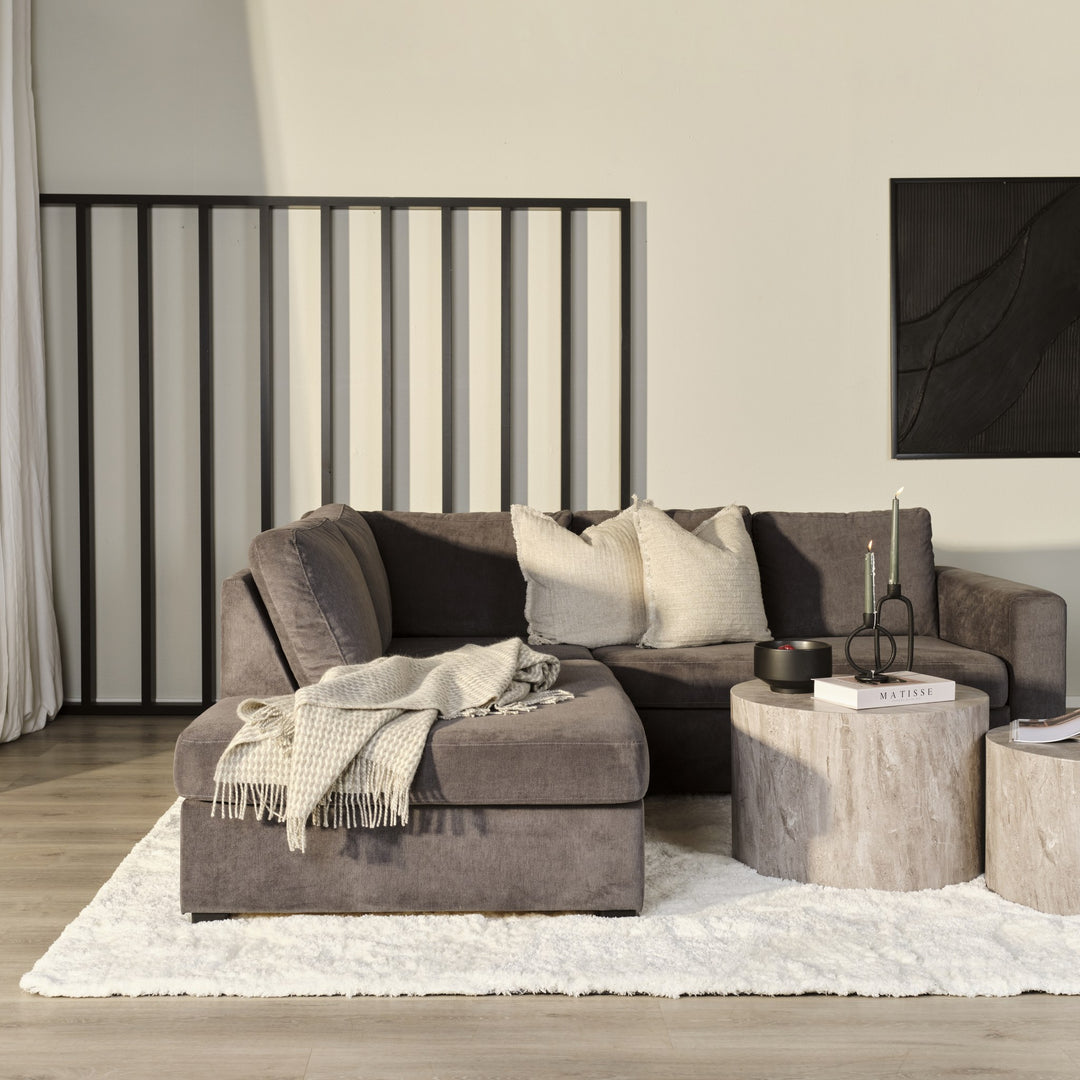 Oslo hjørnesofa i mørk gråbrun velur i stue med to runde travertinbord, beige puter og panelvegg