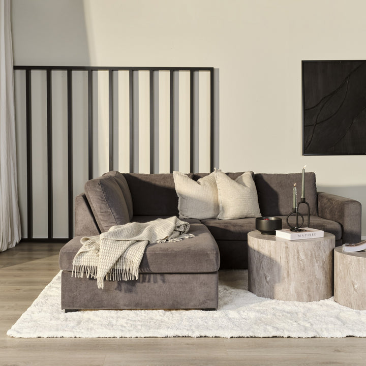 Oslo hjørnesofa i mørk gråbrun velur i stue med to runde travertinbord, beige puter og panelvegg