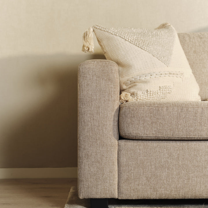 Oslo hjørnesofa i beige, nærbilde av armlene med kremhvit pute mot beige vegg