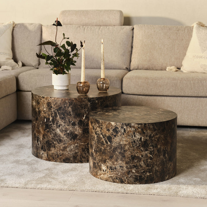 Oslo hjørnesofa i beige bak to runde sofabord i brun marmor med grønn plante og lys.