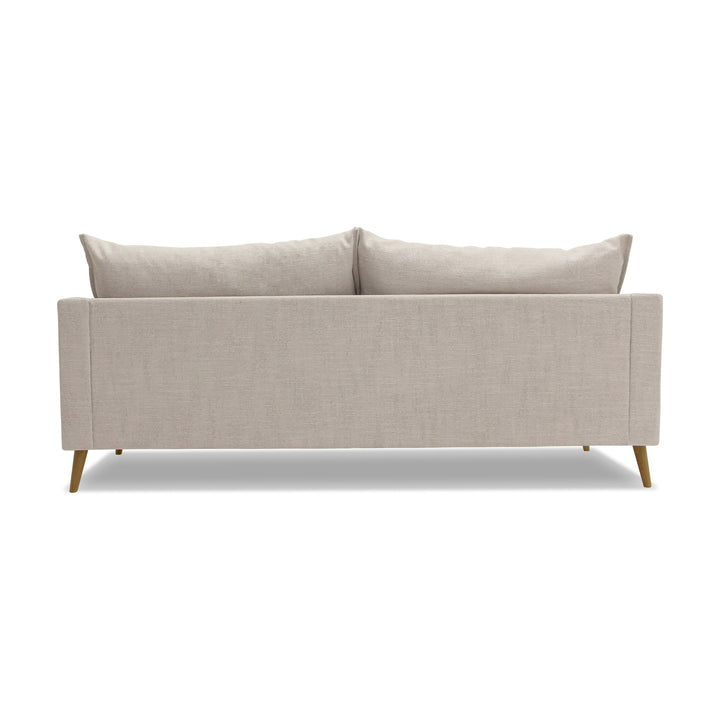Justin sofa i lys beige stoff med løse ryggputer og treben, sett bakfra.
