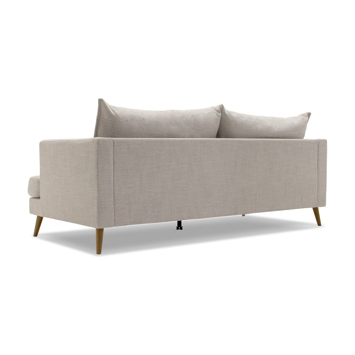 Justin sofa i lys beige stoff med løse ryggputer og treben, sett skrått bakfra.