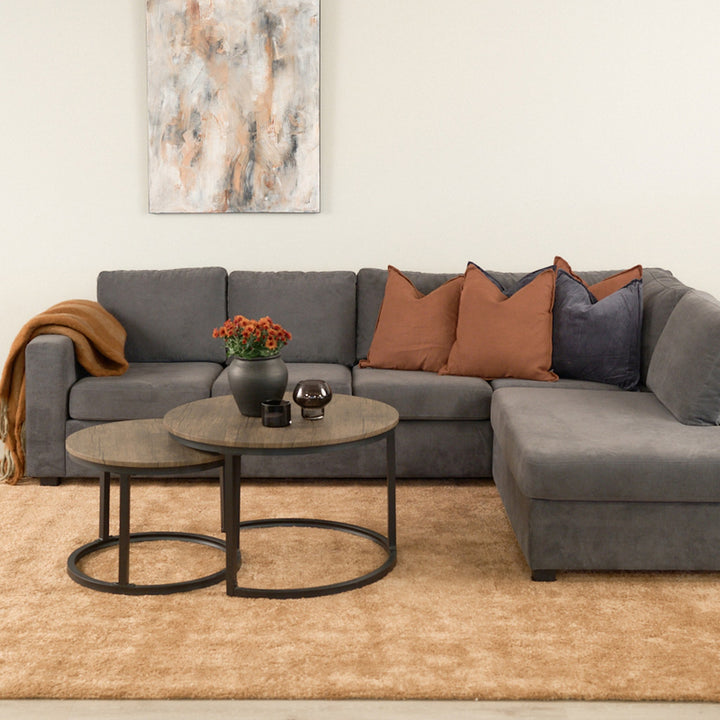 Viken hjørnesofa i mørk grå stoff i stue med abstrakt bilde, runde sofabord og beige teppe.