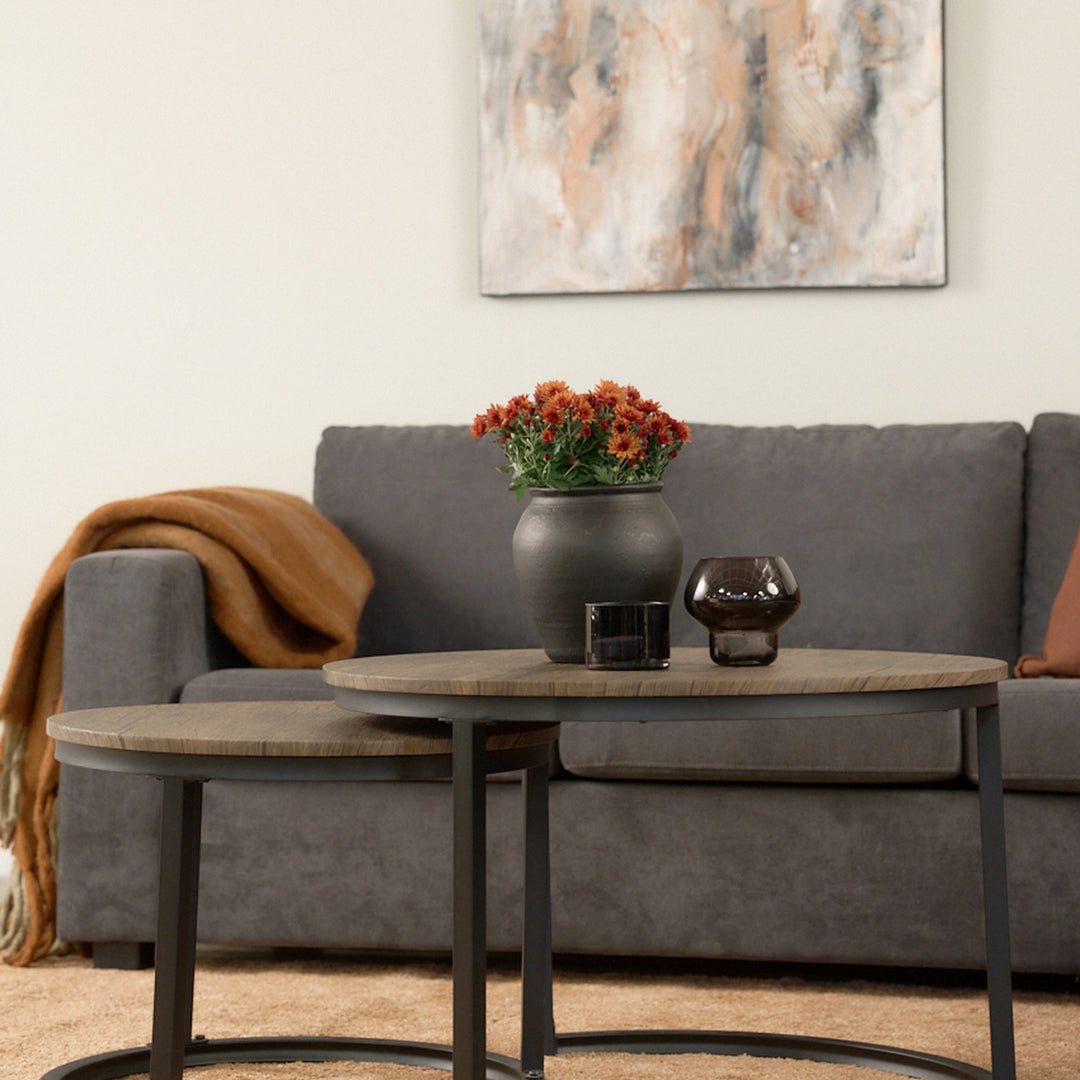Viken hjørnesofa i mørk grå stoff bak runde sofabord med oransje blomster, i lys stue.
