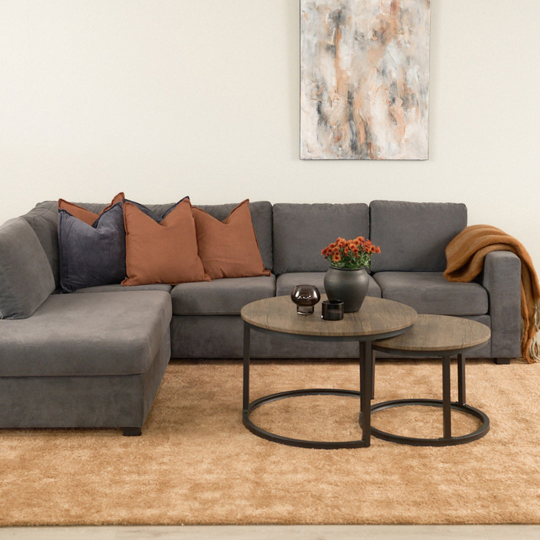 Viken hjørnesofa i mørk grå stoff med rustfargede puter, runde sofabord og beige teppe.