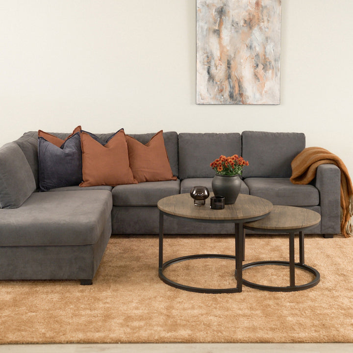 Viken hjørnesofa i mørk grå stoff med rustfargede puter, runde sofabord og beige teppe.