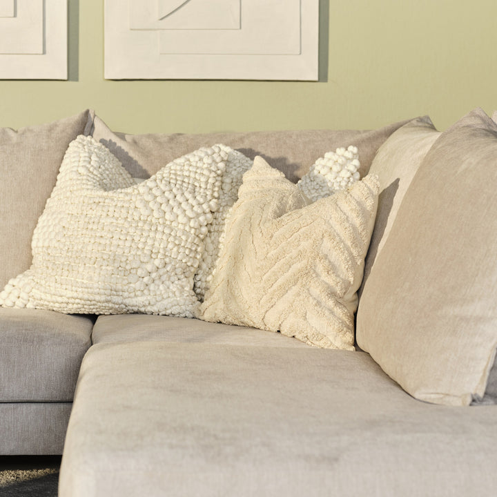 Justin hjørnesofa i beige stoff med kremhvite strukturputer, grønn vegg og innrammet kunst