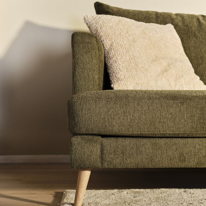 Justin hjørnesofa i olivengrønn stoff med hvit bouclépute, treben og beige vegg