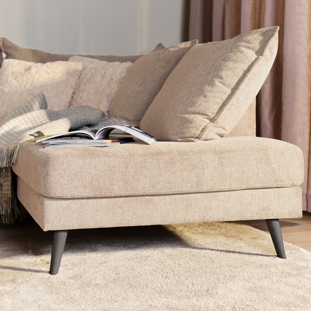 Justin hjørnesofa i beige stoff med puter, pledd og oppslått magasin ved gardin