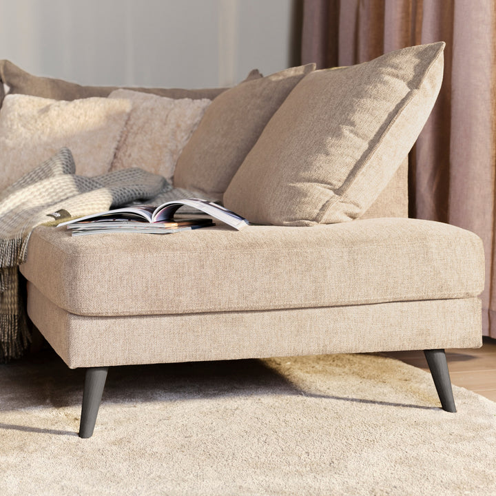 Justin hjørnesofa i beige stoff med puter, pledd og oppslått magasin ved gardin