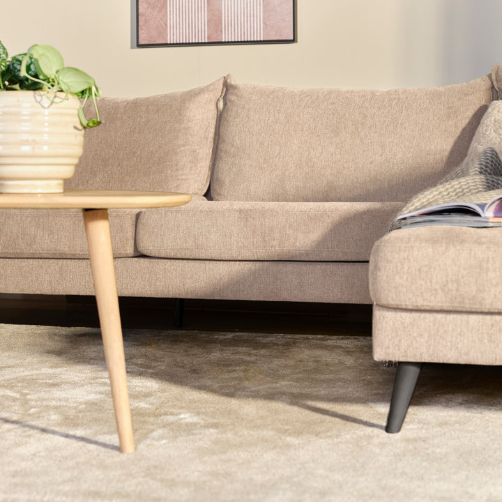 Justin hjørnesofa i beige stoff i stue med trebord, potteplante og innrammet bilde