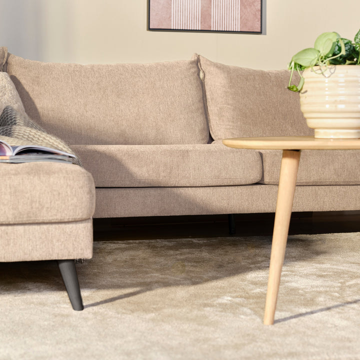 Justin hjørnesofa i beige stoff i stue med trebord og grønn potteplante