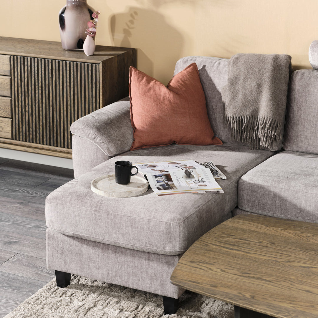 Solution hjørnesofa i greige stoff, nærbilde av sjeselong med terrakottapute, pledd og kaffekopp