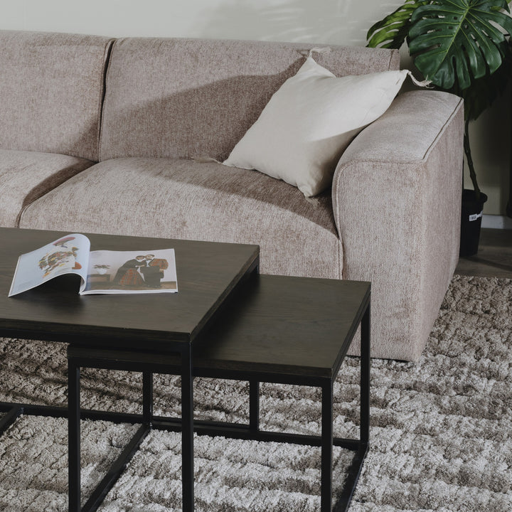 Como hjørnesofa i gråbeige med krempute, sorte sofabord med oppslått magasin på lodnent teppe