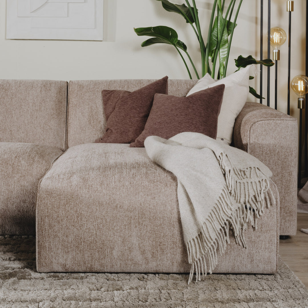 Como hjørnesofa i gråbeige chenille med brune puter og lyst pledd, plante og gulvlampe