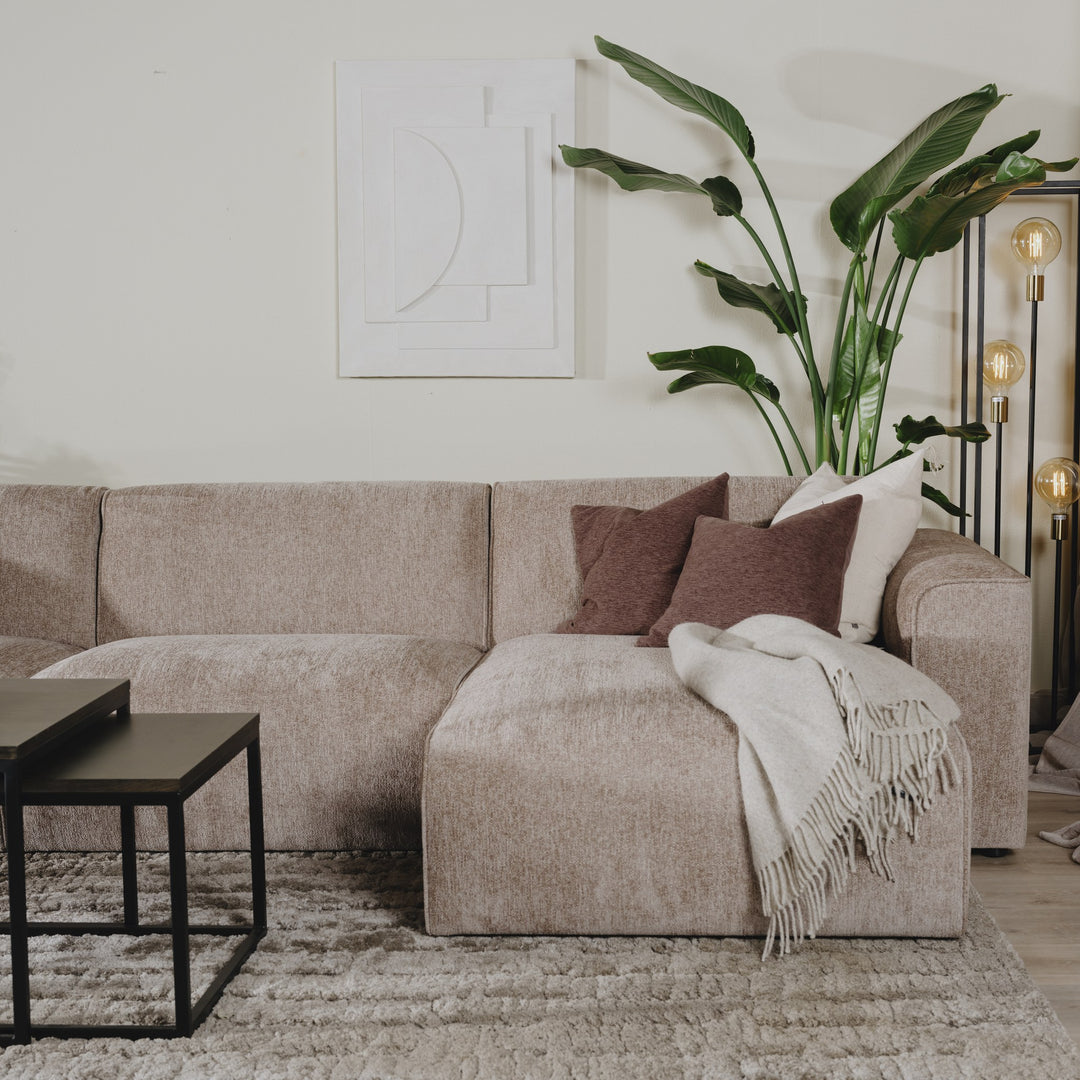 Como hjørnesofa i gråbeige chenille med brun pute og pledd, hvit veggkunst og plante
