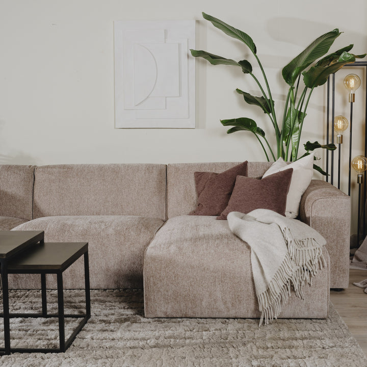 Como hjørnesofa i gråbeige chenille med brun pute og pledd, hvit veggkunst og plante