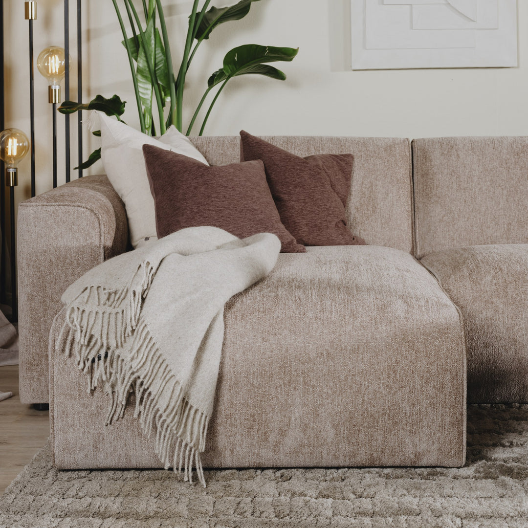 Como hjørnesofa i gråbeige chenille med brune puter og lyst pledd, plante og gulvlampe